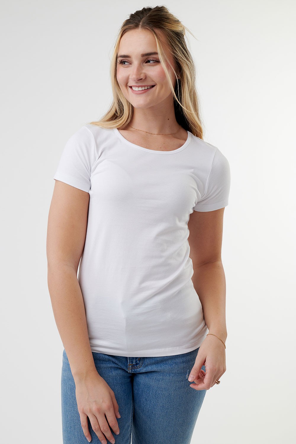 Smiling blonde woman wearing a fitted white short-sleeve crew neck t-shirt with blue jeans against a white background